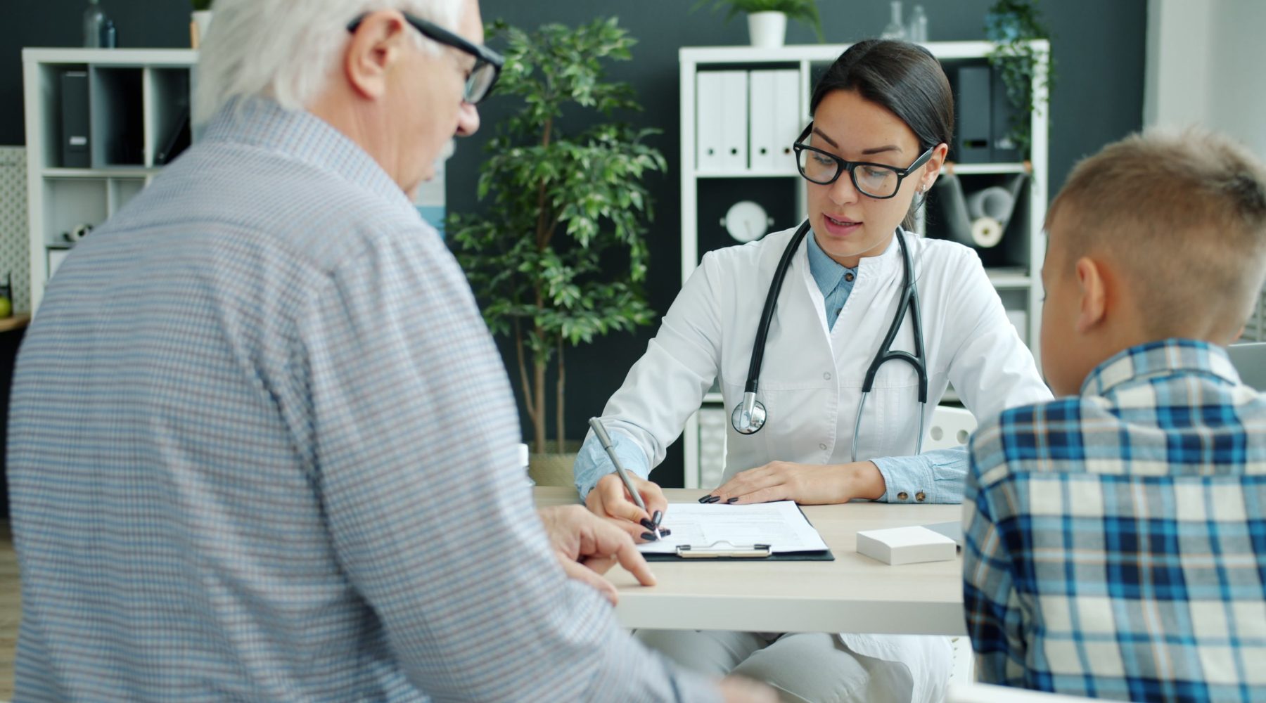 Hausärztin im Gespräch mit einem älteren Patienten und einem Kind in der Praxis